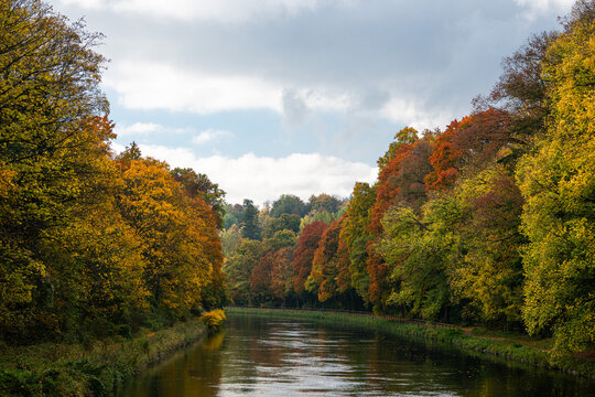 Autumn landscape in warm colours red, orange and yellow around the river under the cloudy blue sky