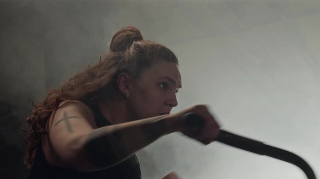Young Caucasian woman with tattoos training intensely on air bike in gym. Footage is ideal for fitness brand commercials, gym advertisements, and motivational athletic campaigns