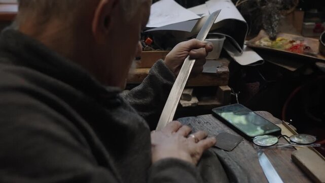 Elderly craftsman working in his old workshop, carefully restoring collectible Japanese bladed weapons