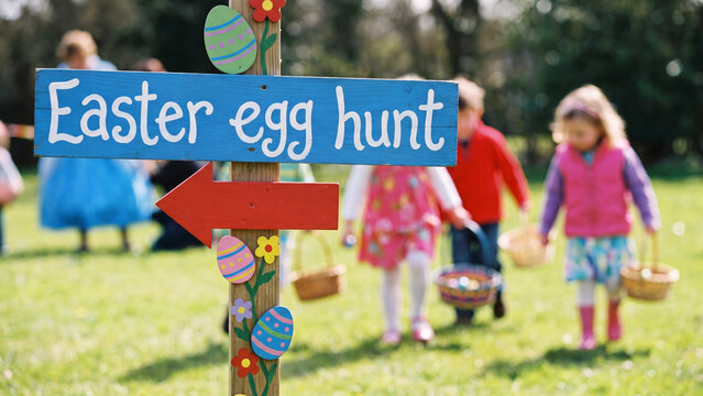 Easter egg hunt signpost with children carrying baskets across grass during a springtime family holiday celebration and seasonal community event