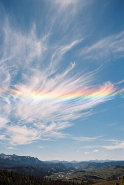 Rare fire rainbow circumhorizontal arc glowing within cirrus clouds over mountain valley