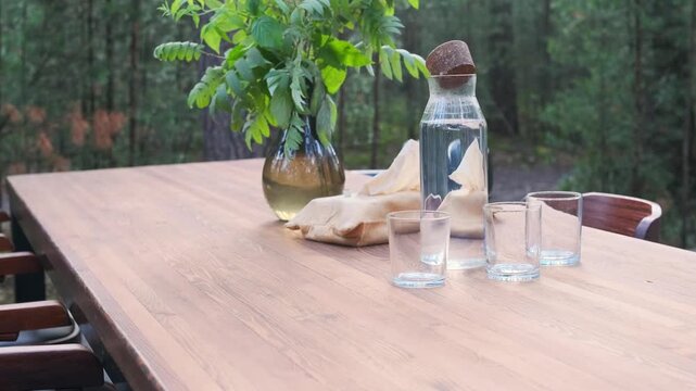 table set with glass water bottle and green branch arrangement in forest cafe. eco-friendly table setting awaits guests in outdoor restaurant. natural dining atmosphere