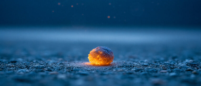 Close up glowing orange sphere on cold, textured ground at night with blue tones and bokeh.