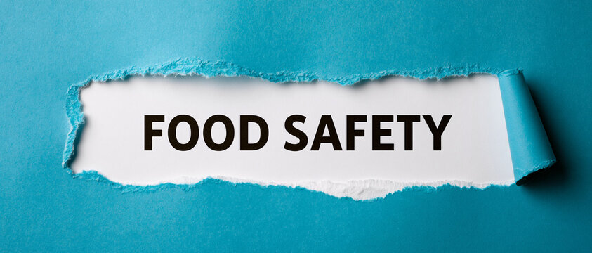 Food safety text written on white paper behind blue torn paper sheet background.