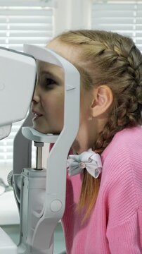 Young girl with braided hair undergoing a vision test at an ophthalmology clinic, her face positioned in an autorefractor for a comprehensive eye exam with an optometrist