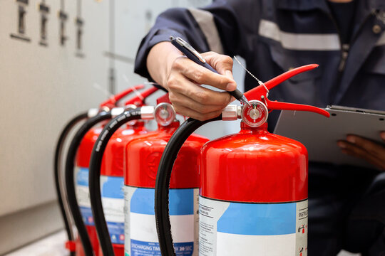 Close up of technician engineer checking pressure gauge of fire extinguisher with pen for annual safety inspection in factory.