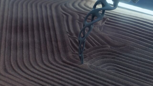 Kinetic table as functional art creates mesmerizing visual display on sand with probe closeup. Device with robotic motors pulls manipulator to draw patterns
