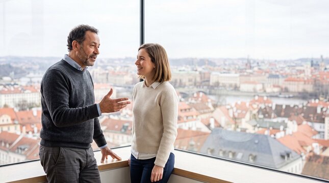 Gesch&auml;ftsmann und Gesch&auml;ftsfrau im Gespr&auml;ch an einer Fensterfront mit Blick &uuml;ber eine Altstadt