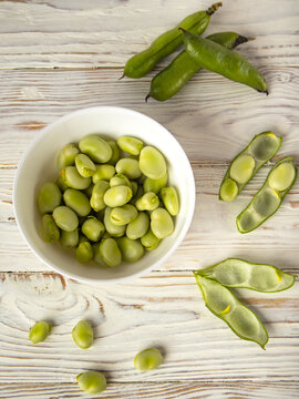 Fresh fava beans in white bowl on wooden table