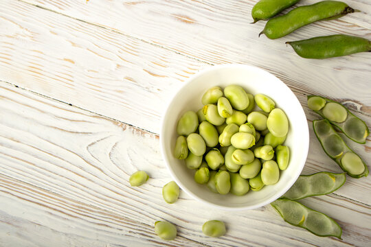 Fresh fava beans in white bowl on wooden table