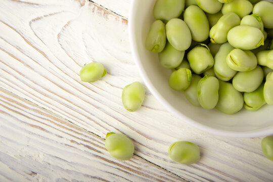 Fresh fava beans in white bowl on wooden table