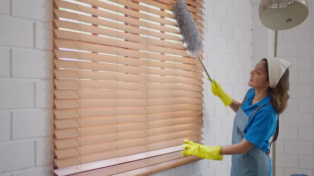 Cleaner woman duster blind window glove apron room dust housework wooden blind cleaning with yellow glove in bright home interior focused hygiene routine