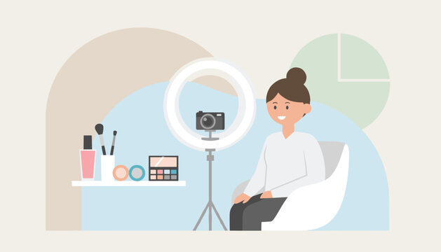 Beauty blogger smiles at a camera inside a ring light during a makeup tutorial video recording in her studio.