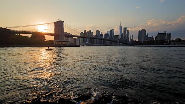 Brooklyn Bridge and Lower Manhattan skyline during sunset in New York, Waterfront video shows One World Trade Center and a jet ski crossing the East River