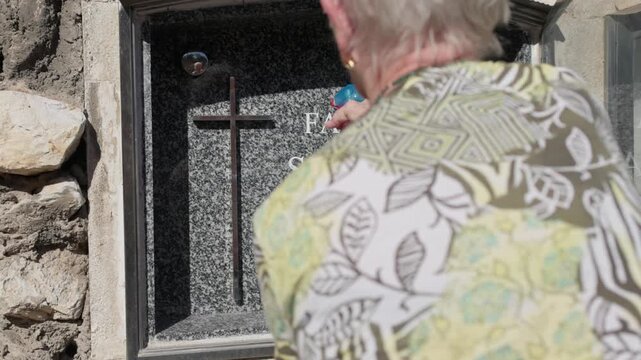 Elderly woman cleaning family gravestone in cemetery