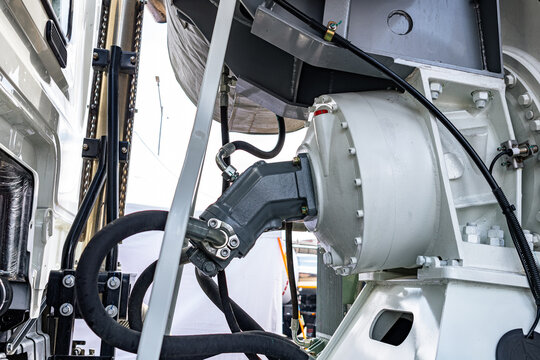 Concrete mixer truck drum hydraulic drive motor assembly. Commercial construction machinery white vehicle chassis frame section with fluid pressure hoses and transport vehicle technical details.