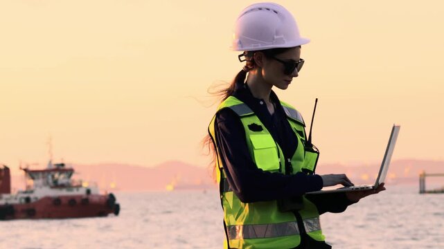Female engineer uniform safety equipment stands surveying the site infrastructure development including the construction port land bridge deep sea port shipyard and container terminal using laptop.