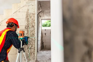 Construction Worker with Laser Level A skilled construction worker, equipped with a hard hat and safety vest, precisely uses a laser level to ensure accurate measurements on a building site. © Chanchai