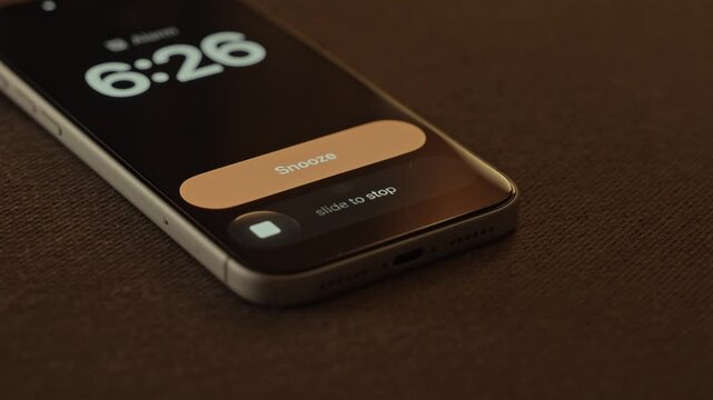 Hand Snoozing Alarm on Smartphone in Bed.

