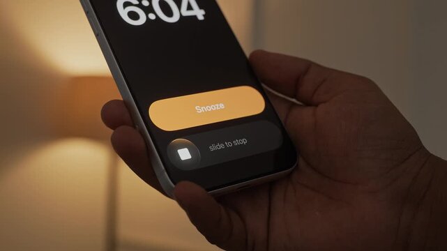 Hand Snoozing Alarm on Smartphone in Bed.
