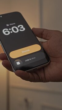 Hand Snoozing Alarm on Smartphone in Bed.
