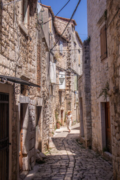 Beautiful blonde young female traveler wearing straw sun hat sightseeing and enjoying summer vacation in an old traditional costal town at Adriatic cost, Croatia.