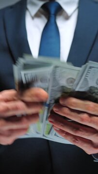 Formally dressed man is counting US Dollar bills, close-up.