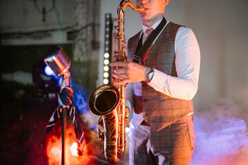 Obraz premium A jazz musician plays a gold saxophone on stage, surrounded by vibrant spotlights, atmospheric smoke, and a vintage microphone during a live evening concert