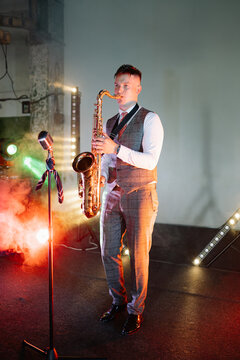 A professional saxophonist in a grey suit performs on a smoky, dimly lit stage with vibrant red and green spotlights