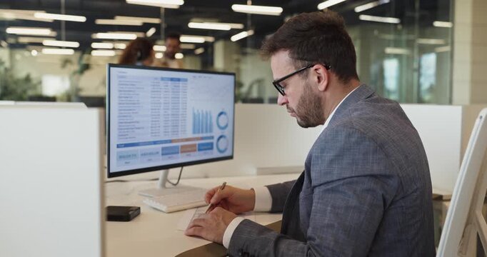 Businessman manager analyst reviewing analytics spreadsheet charts. In office he analyzes data on laptop and screen preparing reports and checking metrics. Core analytics and reporting concept.