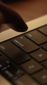 Finger Pressing Caps Lock Button on Laptop Keyboard in Warm Lighted Room.
