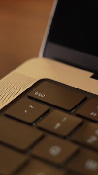 Finger Pressing Escape Key on Laptop Keyboard in Warm Lighted Room
