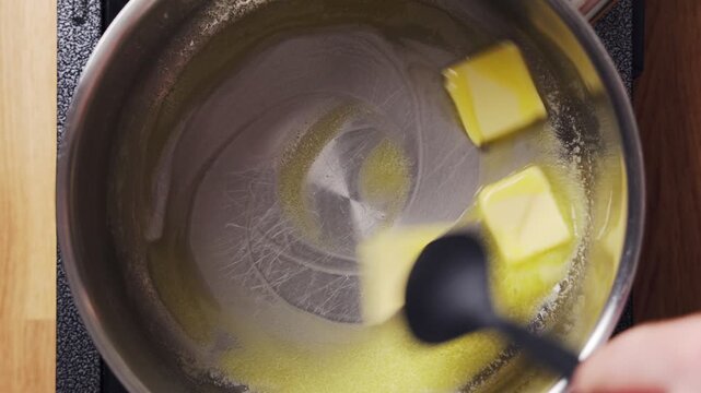 Silicone spoon stirs butter pieces, melting slowly in saucepan. Melted butter creates rich, nutty sauce for pasta or gnocchi. Butter sauce brings simple elegance to homemade Italian dinner.