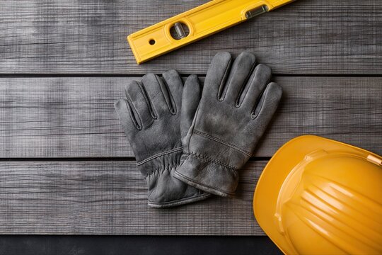 Overhead shot of construction safety gear including a yellow hard hat, work gloves, and a spirit level on a weathered wooden surface.