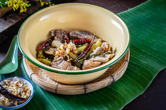 Traditional Northern Thai Jor Pak Kad soup with pork and mustard greens in a vintage enamel bowl on banana leaf. Authentic local dish with sour tamarind, herbs, and fried chili. 