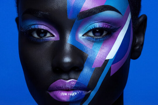 Woman with colorful face paint standing against a blue background during a makeup event in a studio setting