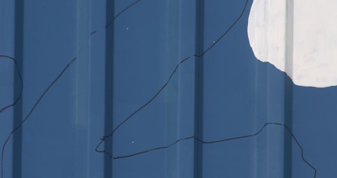 Blue corrugated wall with thin black lines drawn and white paint shape close up