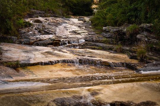 Cascading waterfall Cachoeira dos Macacos flowing over rock cliffs into a calm pool in Ibitipoca, Minas Gerais, Brazil