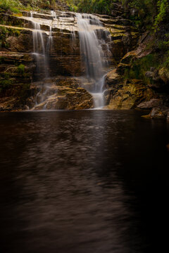 Cascading waterfall Cachoeira dos Macacos flowing over rock cliffs into a calm pool in Ibitipoca, Minas Gerais, Brazil