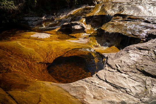 Clear golden river flowing through a lush green valley under a blue sky in Ibitipoca, Minas Gerais, Brazil