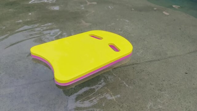 Yellow kickboard floats gently in shallow water on sandy beach