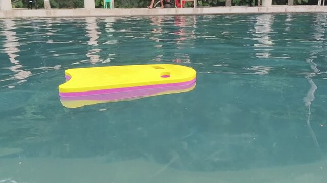Yellow float board gently bobs on calm pool water surface