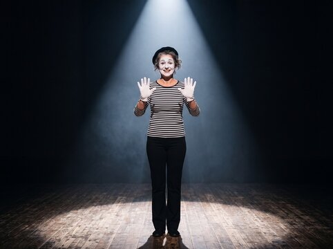 Weibliche Pantomime mit wei&szlig; geschminktem Gesicht und wei&szlig;en Handschuhen auf einer B&uuml;hne im Scheinwerferlicht