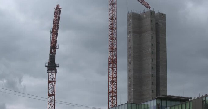 Crane boom arm rotates slowly next to tower block building skyscraper under construction