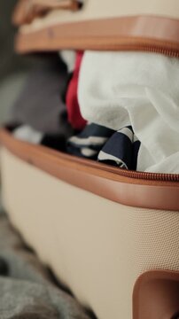 Close up of hands opening an overpacked suitcase with poorly organized clothes after unsuccessful packing attempt before travel or relocation, vertical