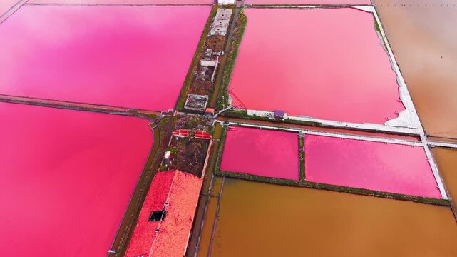 Overhead shot of pink salt pond and red roof warehouse, Bulgaria. Drone perspective shows a canal, walkway and amber colored pool.