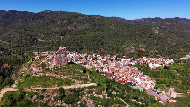 Panoramic view of Azuebar village in Sierra de Espadan natural park, Valencia, Spain, featuring medieval castle ruins on hilltop surrounded by lush Mediterranean forest