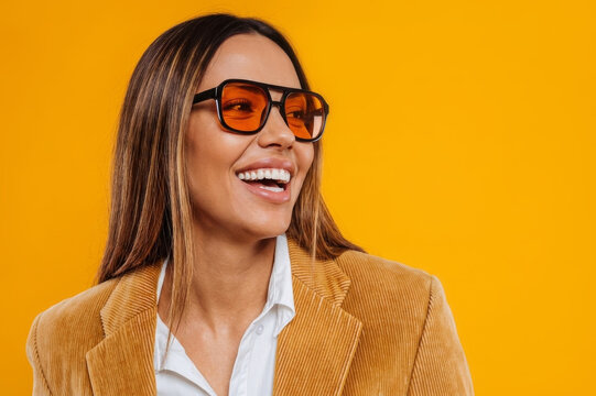 Portrait of a stylish young woman wearing oversized sunglasses with orange-tinted lenses and a mustard yellow corduroy blazer