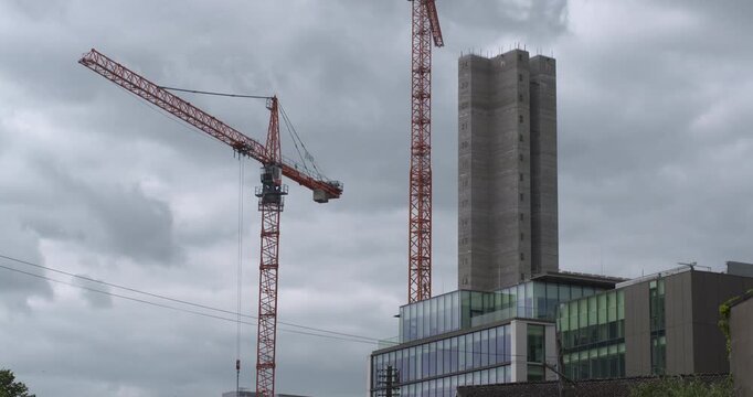Two large cranes next to tower skyscraper building under construction boom arm rotates