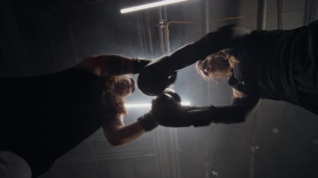 Two Caucasian young women touching boxing gloves and sparring in gym, low angle slow motion shot. Footage ideal for female empowerment campaigns and fitness brand advertisements